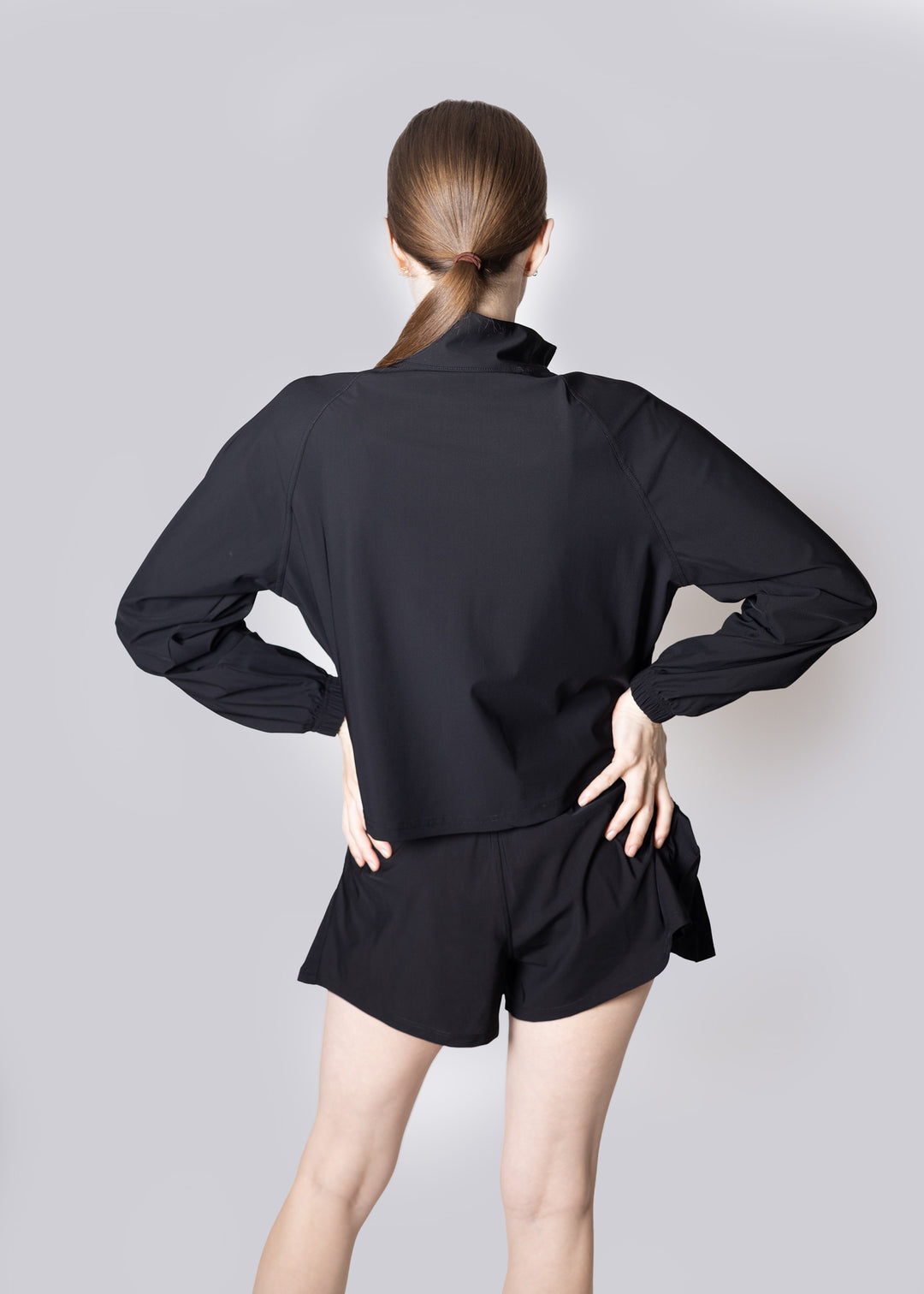 A woman wearing a black outfit with a high collar and shorts on a plain background