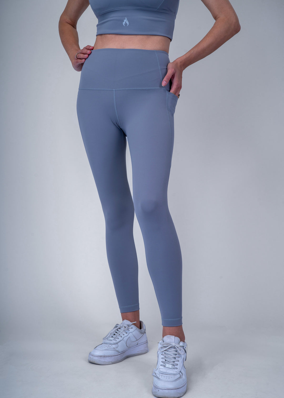 A woman wearing  light blue athletic leggings and a sports bra on a light gray background