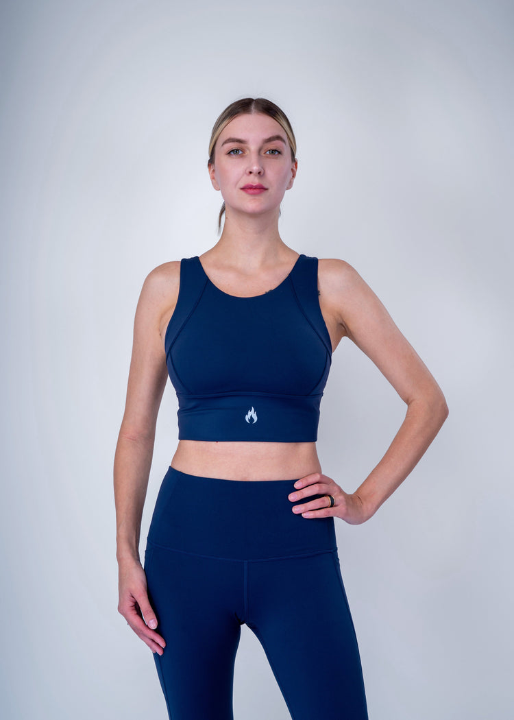 Woman wearing a navy blue sports bra and leggings with a white Spofire logo on a light gray background 