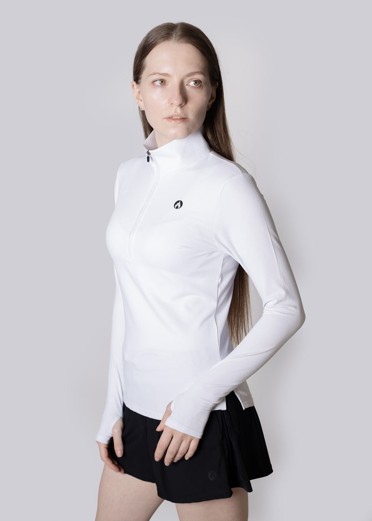 A woman wearing a white long-sleeve athletic top with a logo on a light gray background and Black shorts.