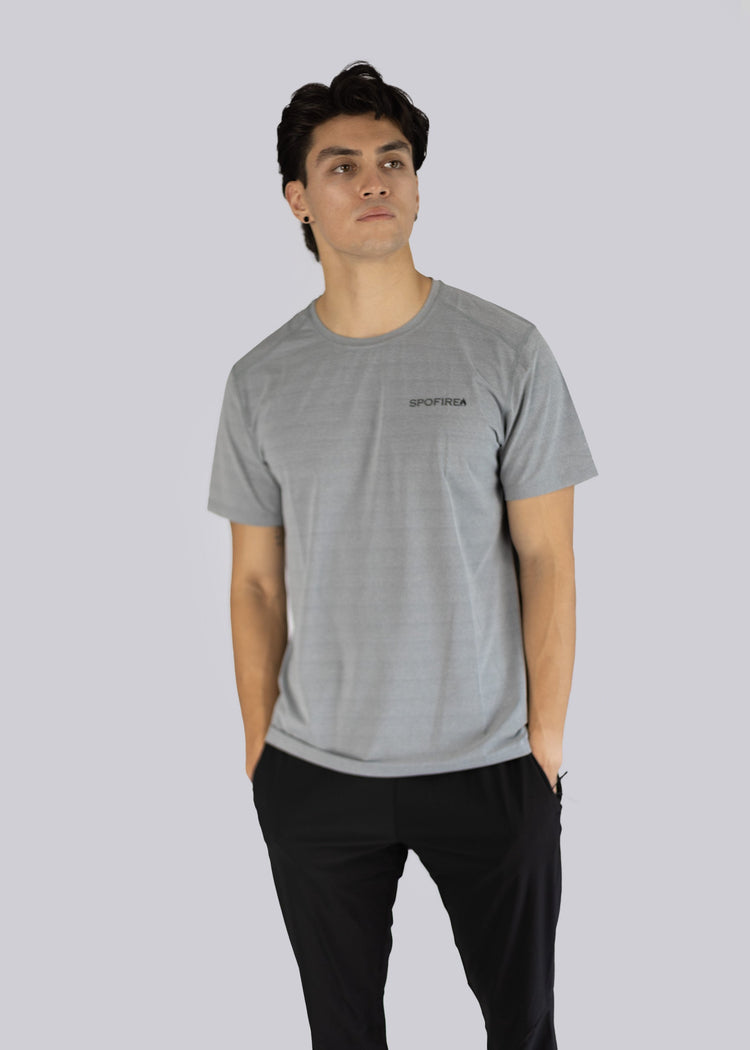 A man wearing a gray t-shirt with the Spofire logo on a light gray background, hands inside his pants pockets