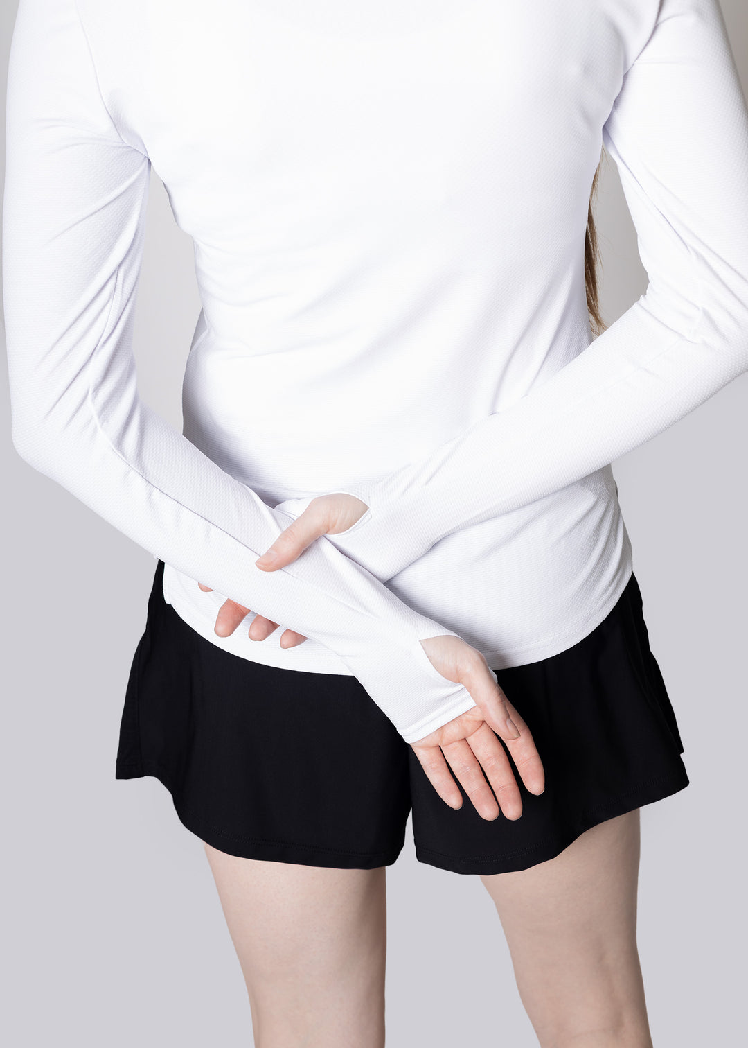 A woman  wearing a white long-sleeve top and black shorts on a light gray background