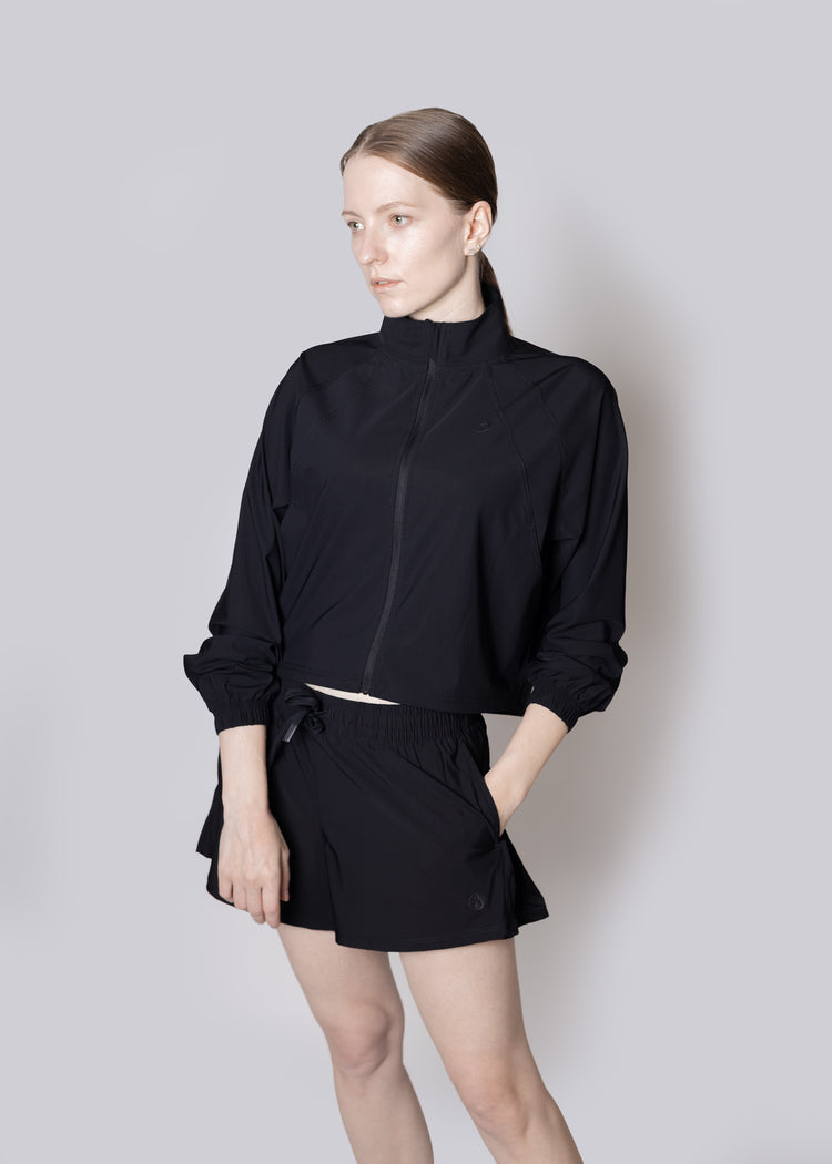 A woman wearing a black outfit against a plain background, Jacket and Shorts