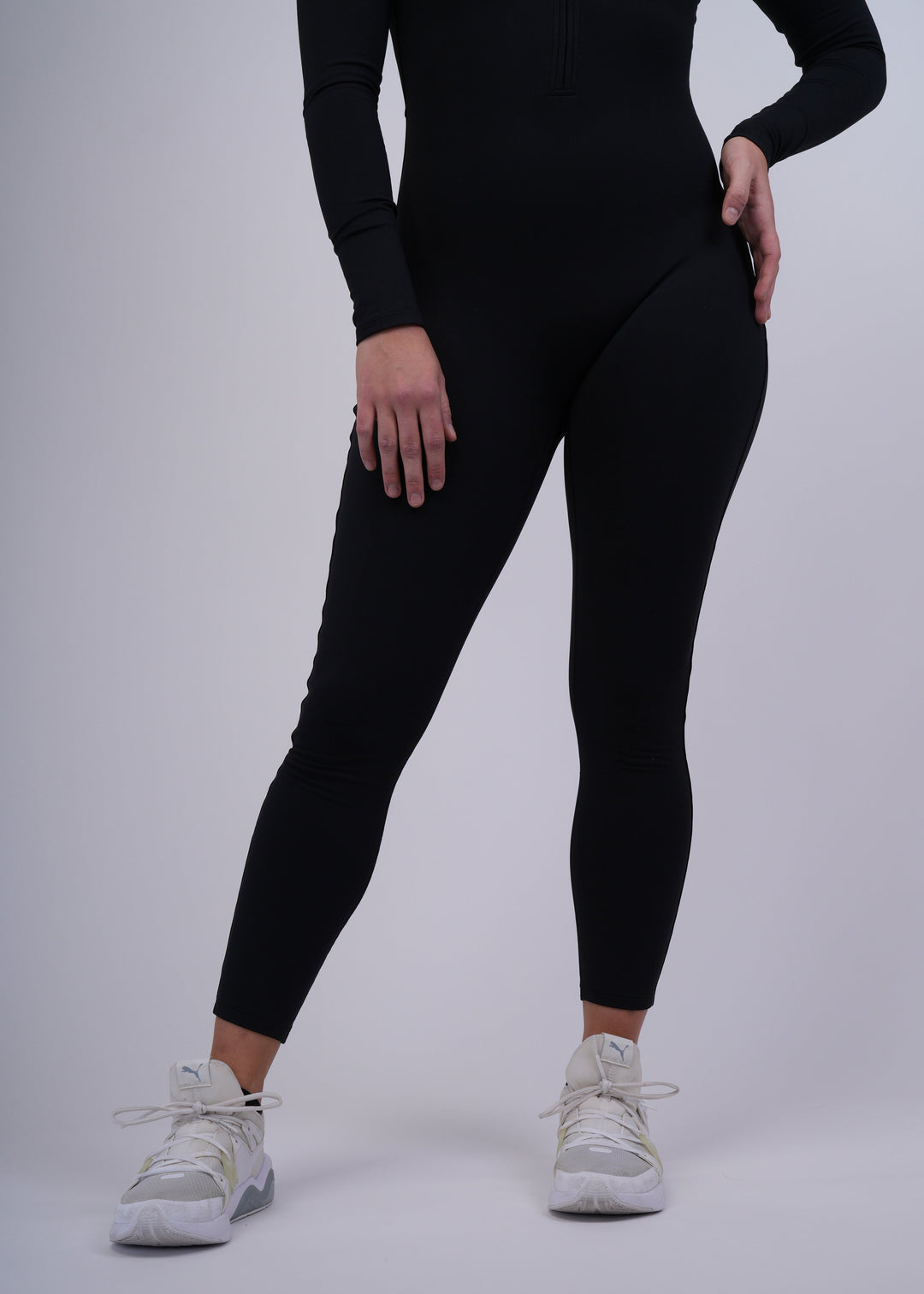 A model wearing a black Spofire bodysuit and white sneakers on a gray background