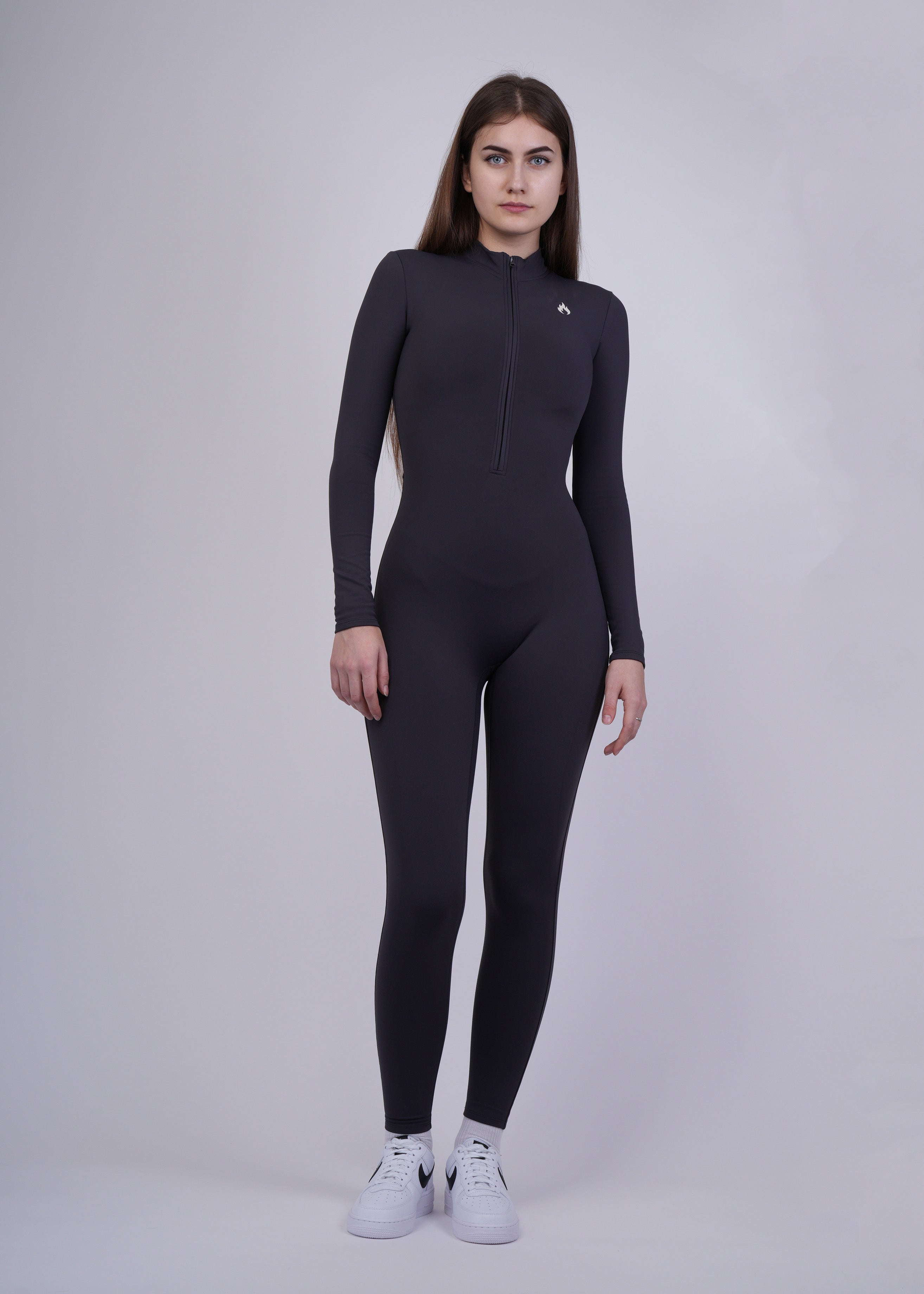 A woman wearing a black full-body suit on a gray background, front shot