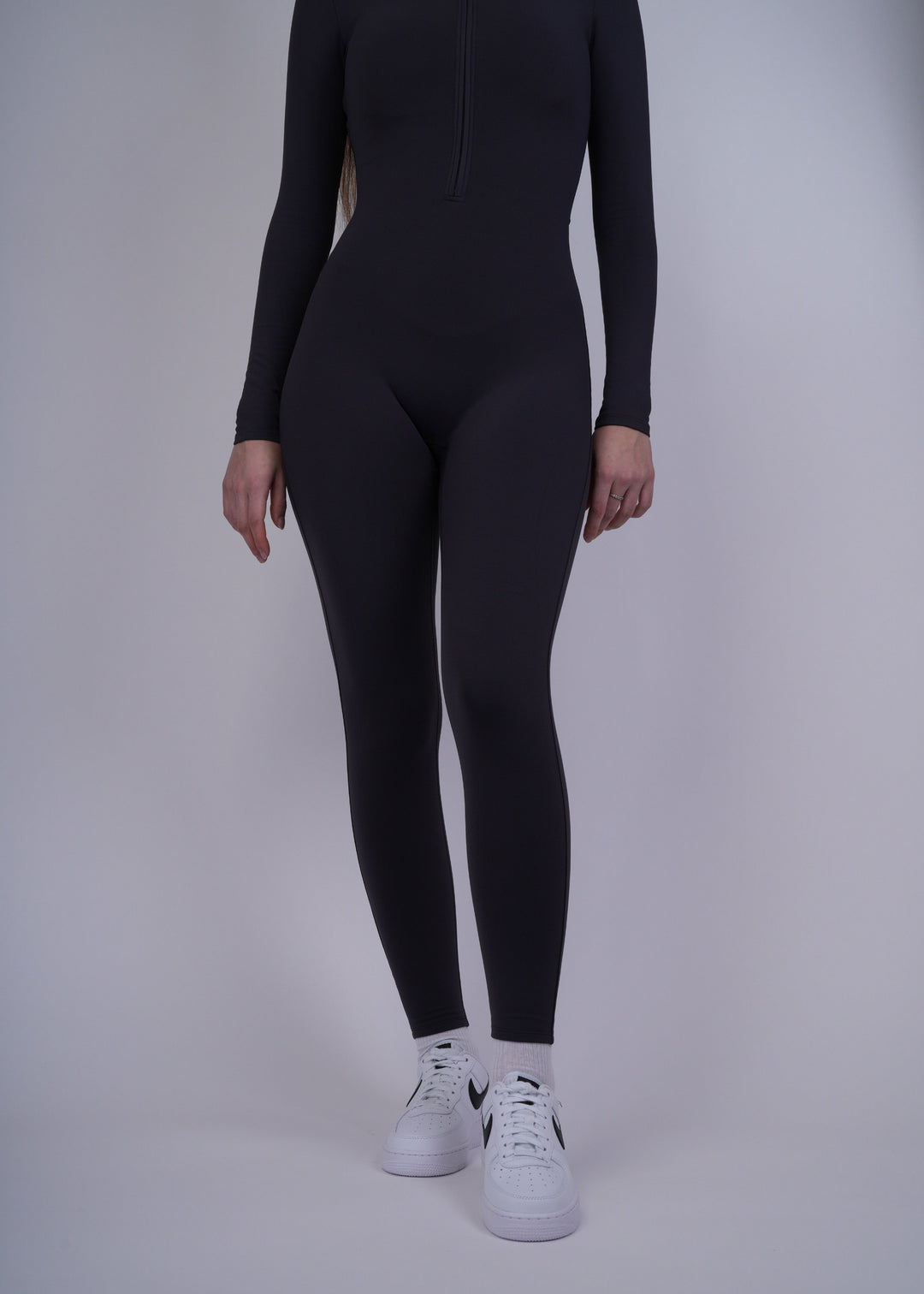 A model  wearing a black bodysuit and white sneakers on a plain background
