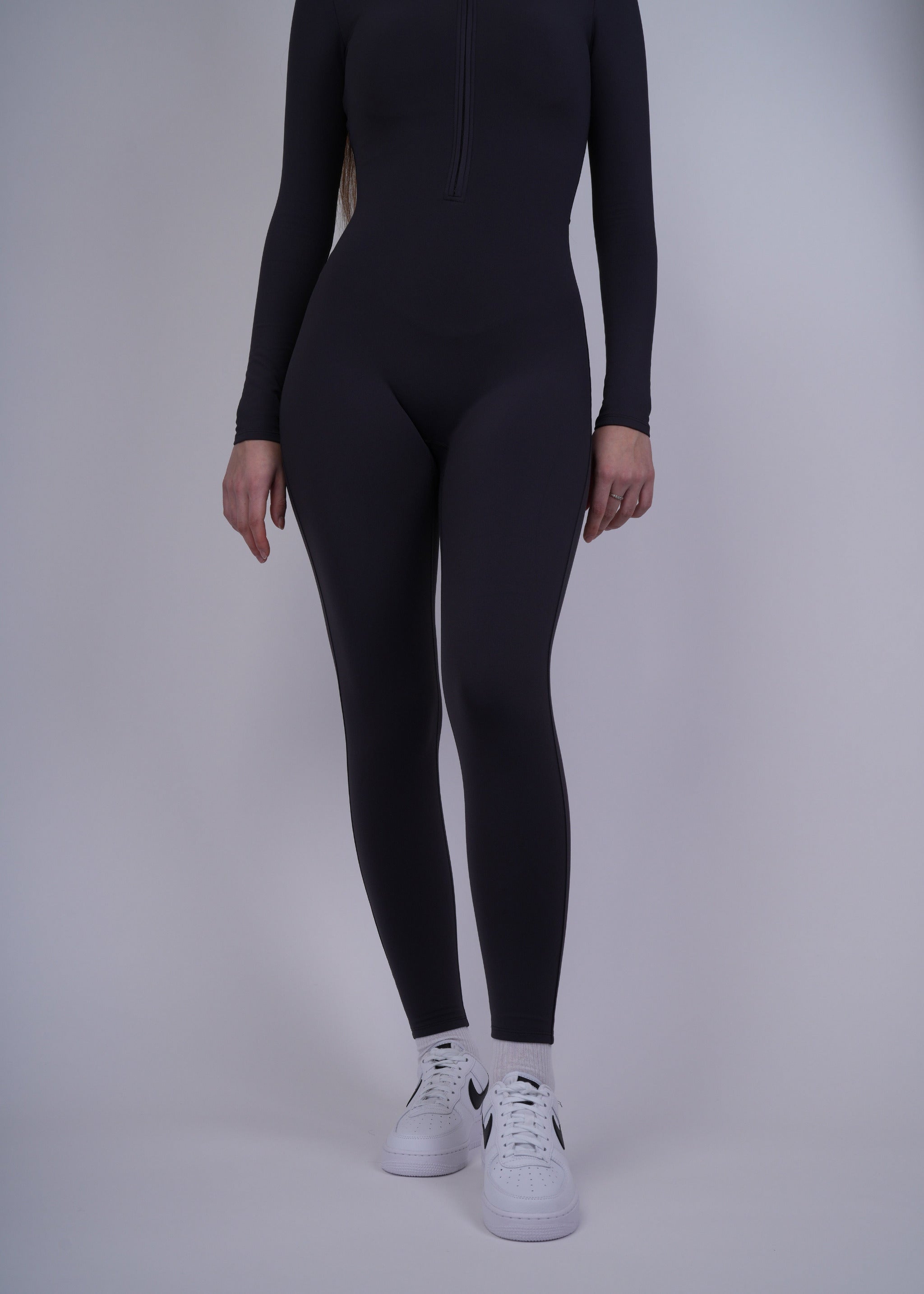 A model  wearing a black bodysuit and white sneakers on a plain background