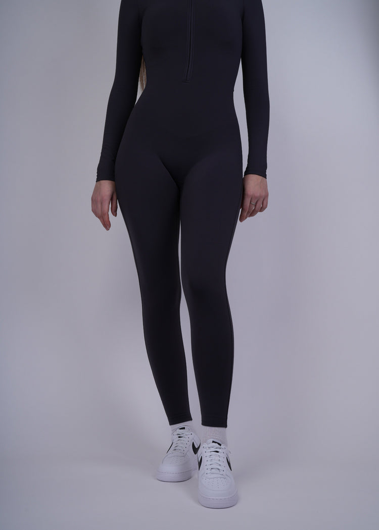 A model  wearing a black bodysuit and white sneakers on a plain background